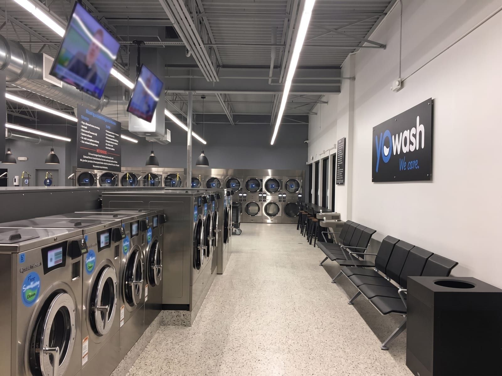 Inside a YoWash laundromat — washers, dryers, smart TVs, and the YoWash 'we care' sign on the wall